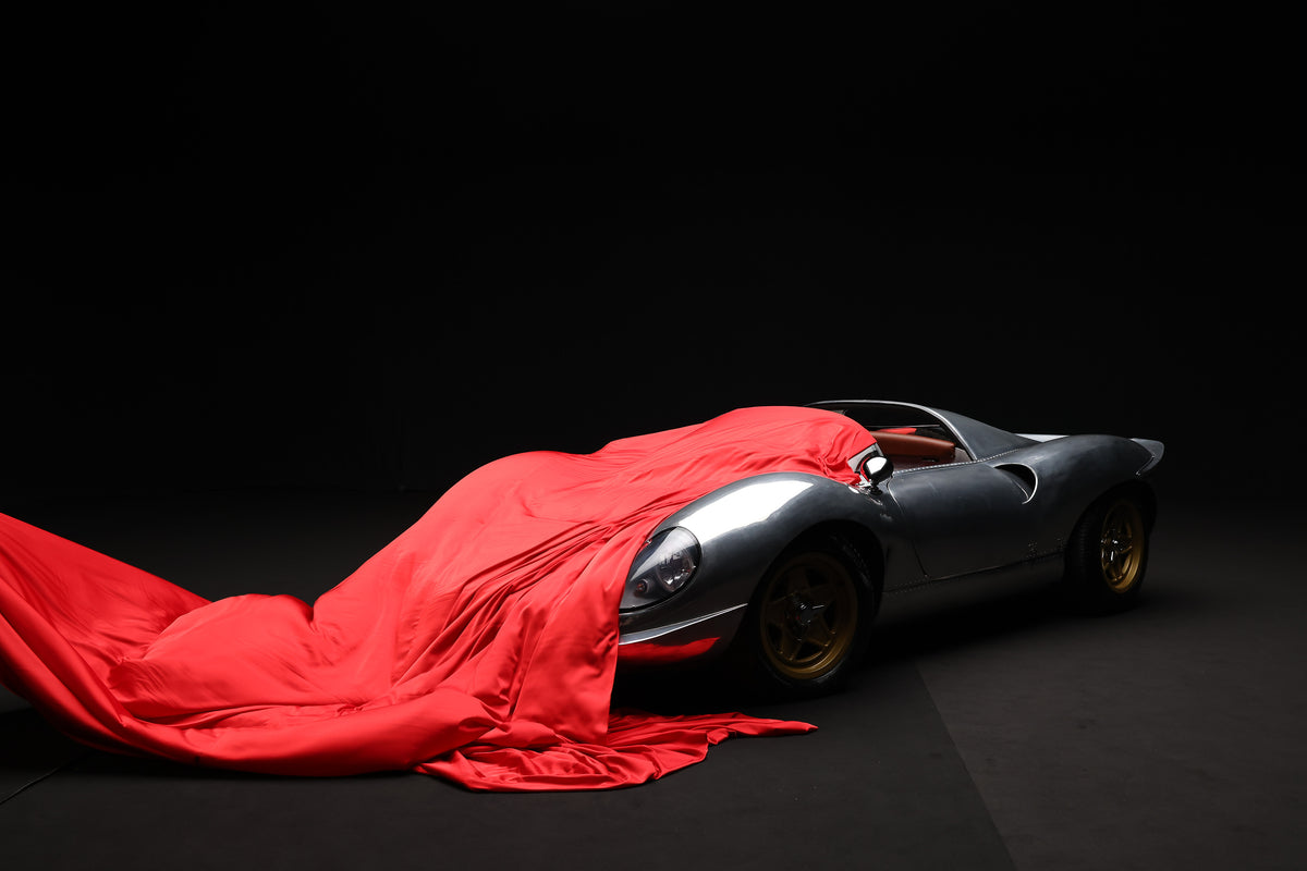A silver racing car half out from under a red silk cover